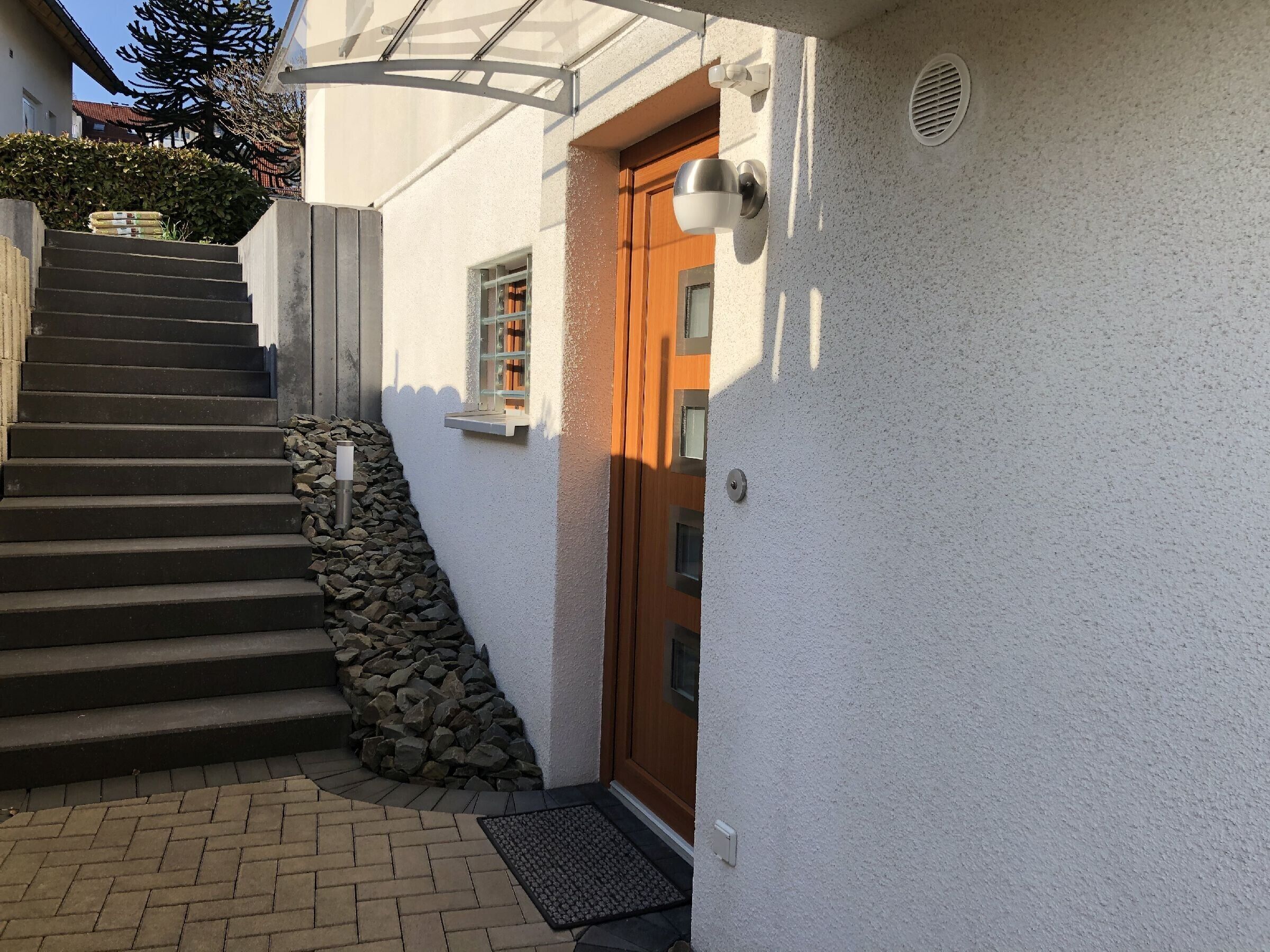 Eine Treppe führt zu einer Holztür, einem kleinen Fenster und einer weißen Wand mit strukturierter Oberfläche.