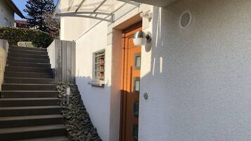 Eine Treppe führt zu einer Holztür, einem kleinen Fenster und einer weißen Wand mit strukturierter Oberfläche.