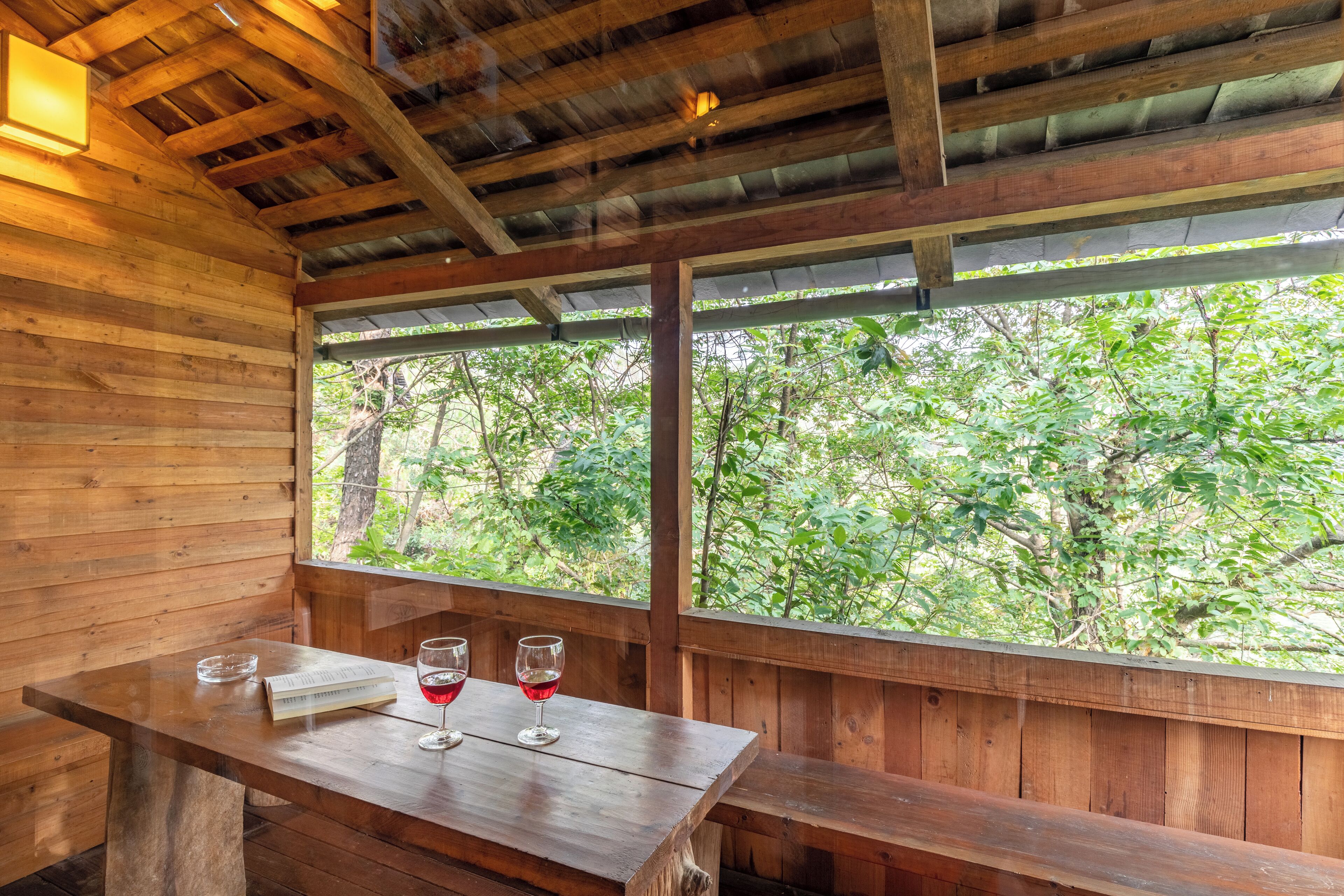 Eine Holzhütte mit Tisch, zwei Weingläsern, davon eines mit Rotwein, und einer Bank.
