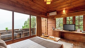 A wooden cabin room with a bed, a TV, and a large window overlooking a forest. - Alaya Stays Suro Woodcrest Chalet (Kandaghat)