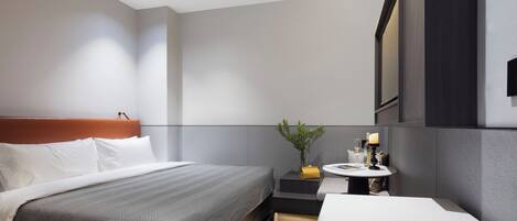 Una habitación de hotel moderna con una cama grande, una mesita de noche con lámpara y un pequeño rincón de descanso.