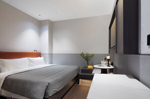Ein modernes Hotelzimmer mit einem großen Bett, einem Nachttisch mit Lampe und einer kleinen Sitzecke.