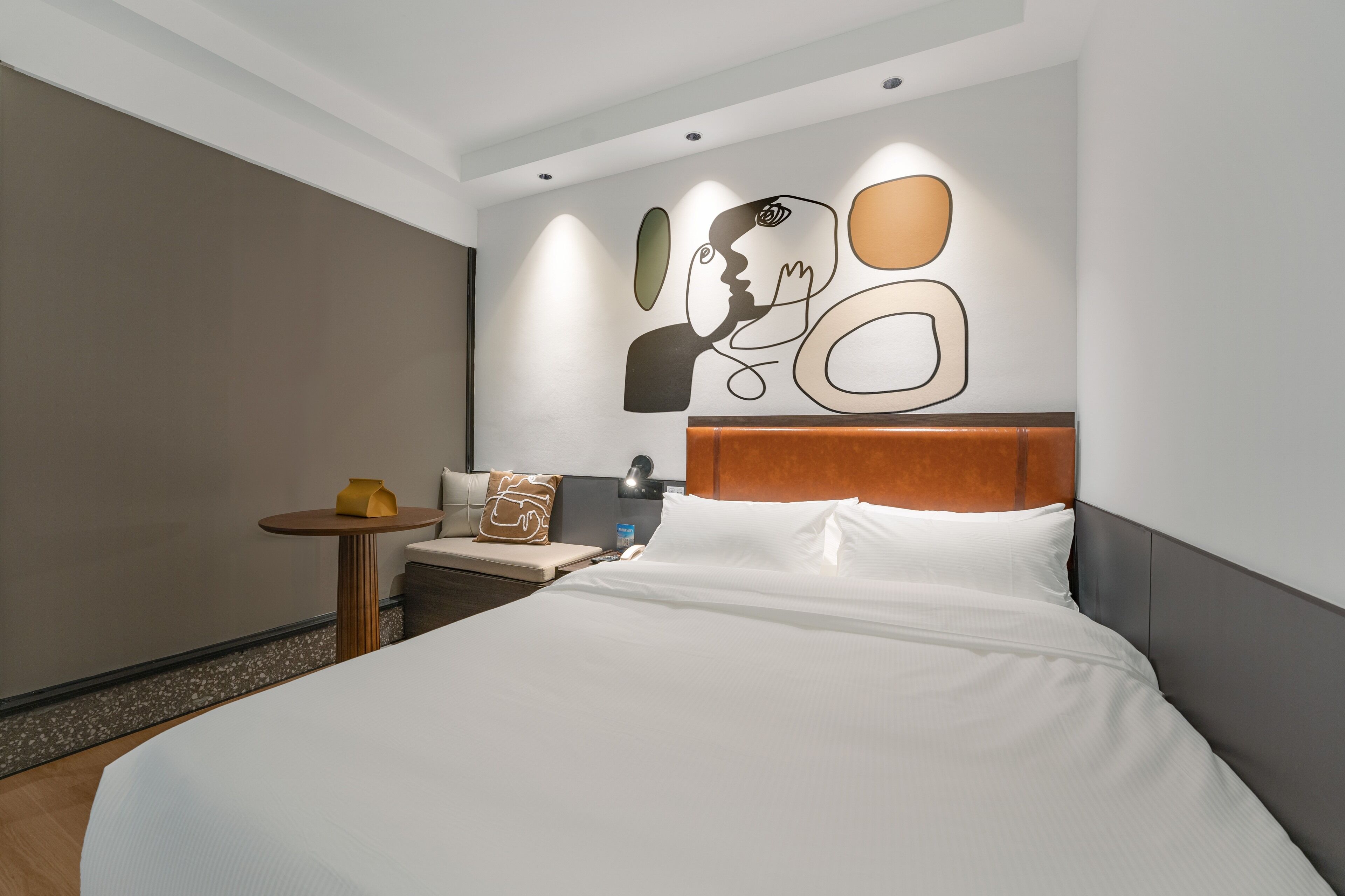 Una habitación de hotel moderna con una cama grande, una mesa redonda pequeña y una original obra de arte abstracta en la pared.