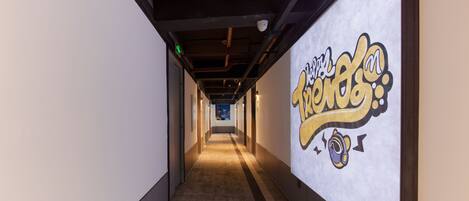A hallway with a mural on the right wall and a ceiling with exposed pipes and lighting fixtures.