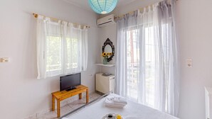 A hotel room with a bed, a TV on a wooden table, an air conditioning unit, a window with sheer curtains, and a decorative mirror with sunflowers. - Alisahni Home 2, Villa (Chania)