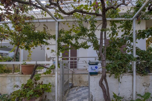 A covered outdoor area with a metal gate, potted plants, and a staircase leading to a building entrance.