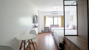 Habitación de hotel con cama, escritorio, silla, televisión y ventana con cortinas.