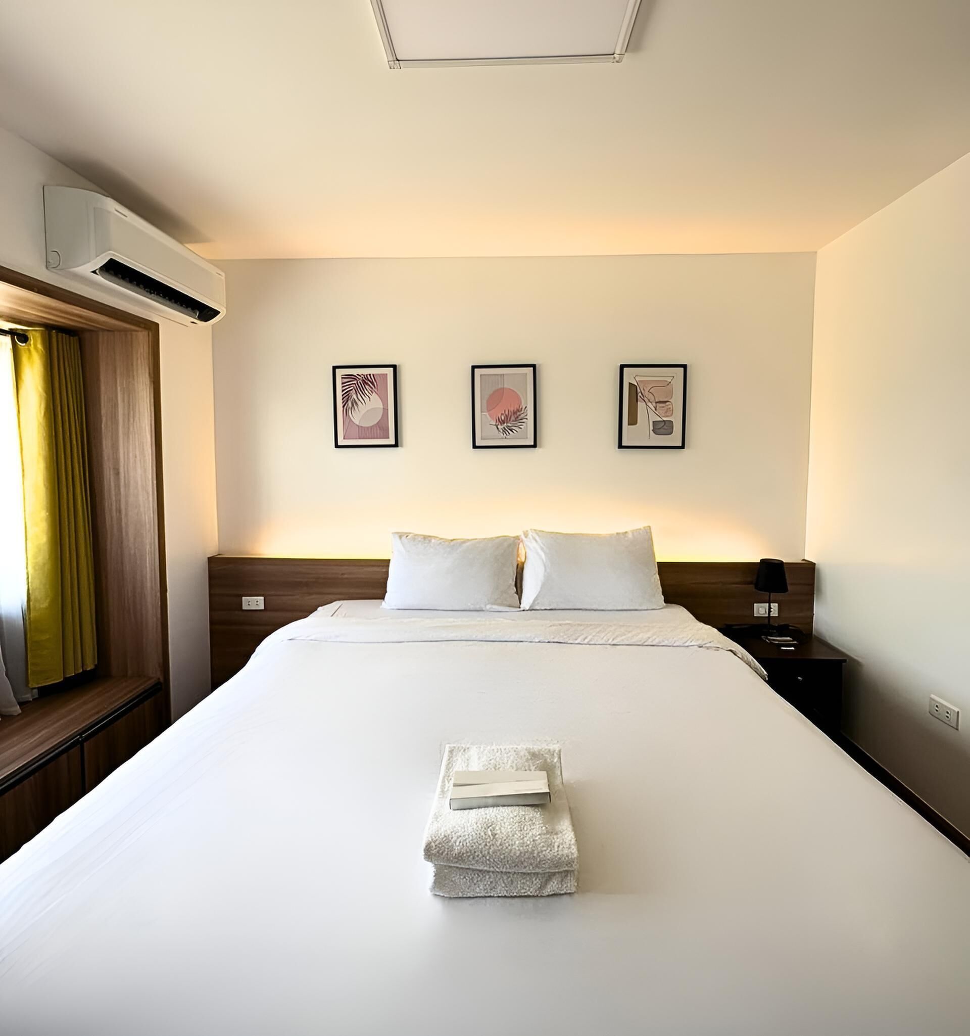 A hotel room with a large bed, two pillows, a nightstand, a lamp, and three framed artworks on the wall.