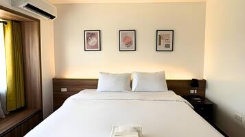 A hotel room with a large bed, two pillows, a nightstand, a lamp, and three framed artworks on the wall.