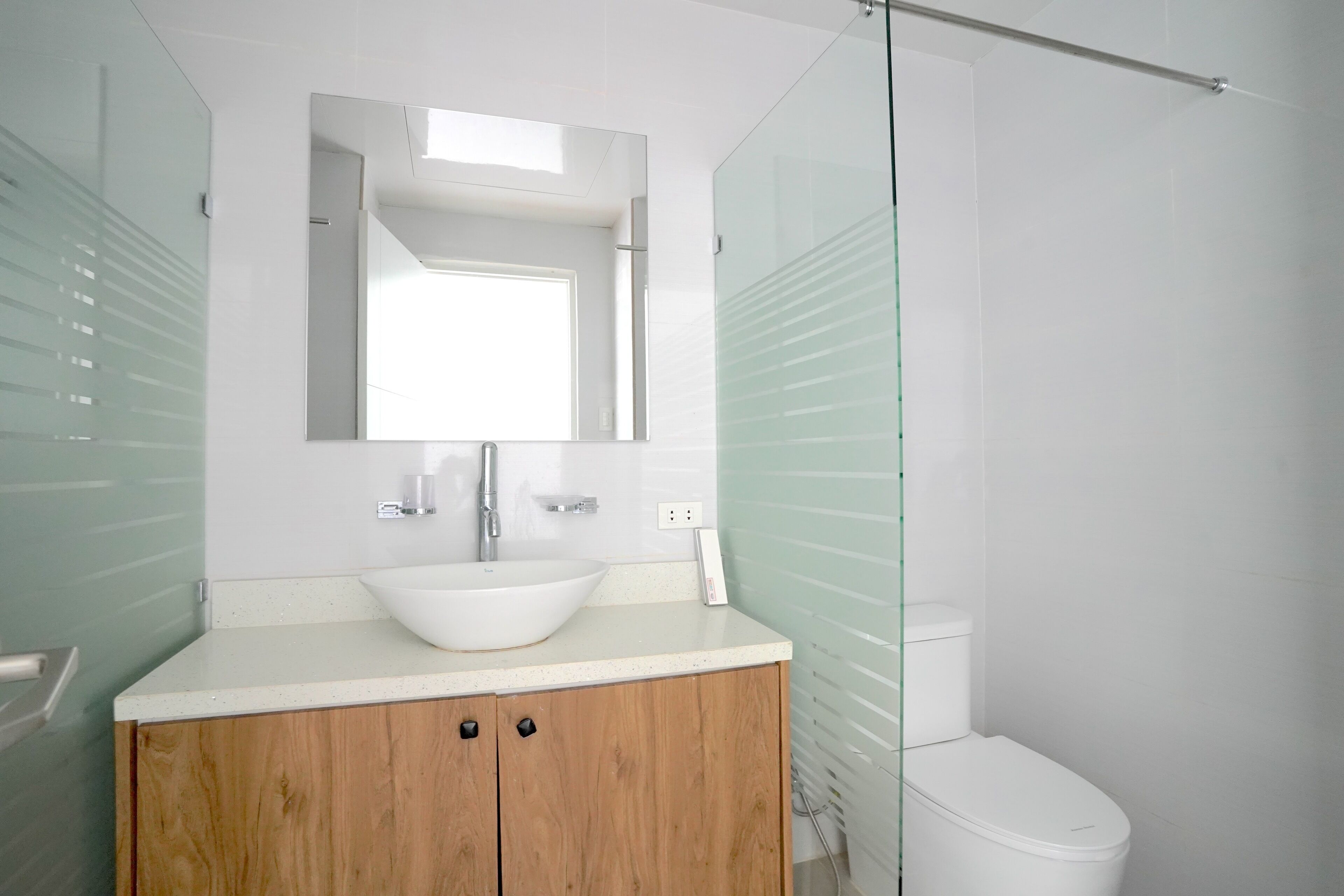 A modern bathroom with a white sink, wooden vanity, and a glass shower enclosure.