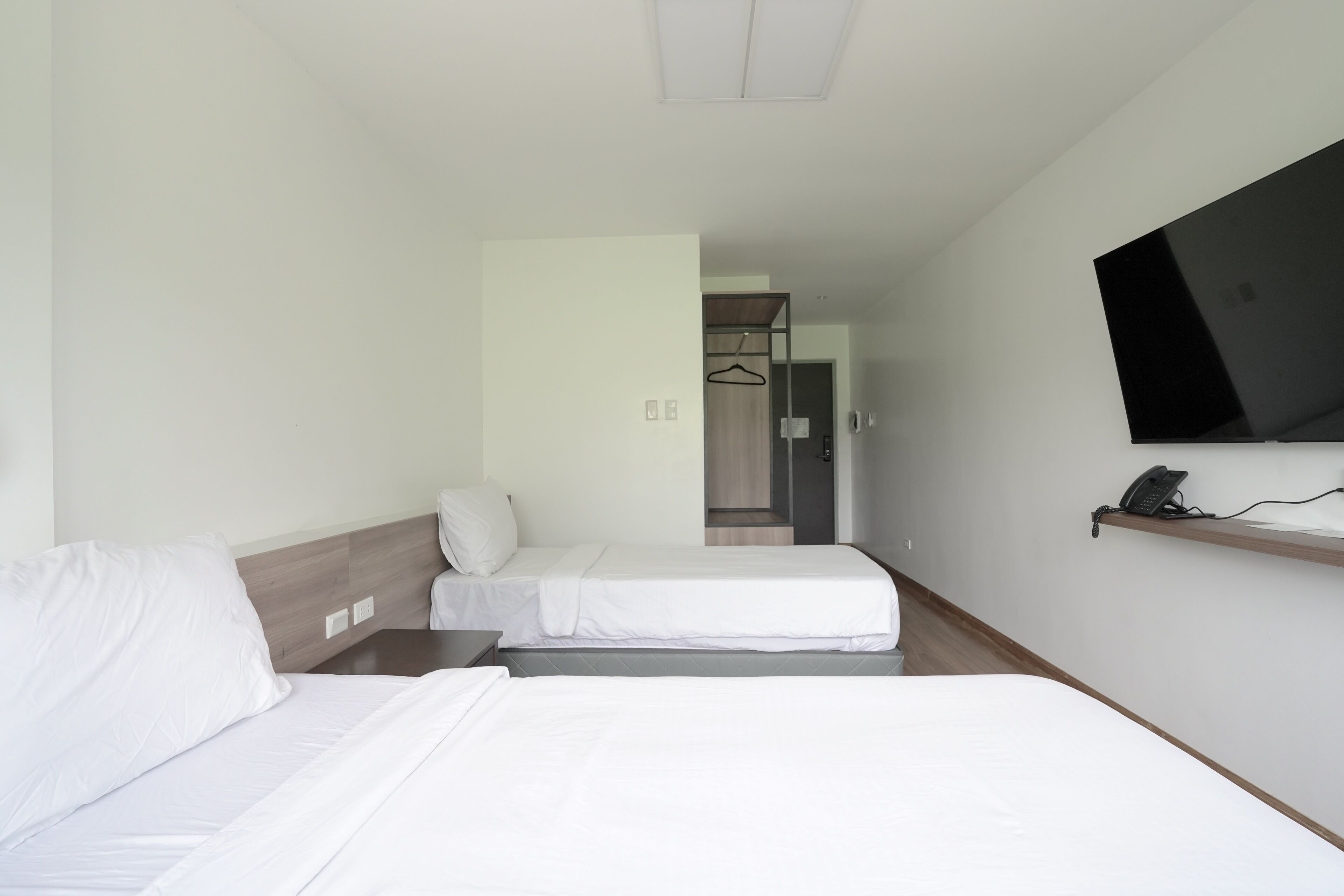 Ein Hotelzimmer mit zwei Betten, einem an der Wand befestigten Fernseher und einem Telefon auf einem Regal.