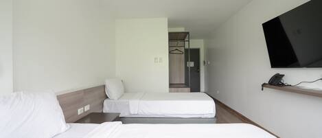 Ein Hotelzimmer mit zwei Betten, einem an der Wand befestigten Fernseher und einem Telefon auf einem Regal.