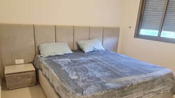 A bedroom with a bed, two pillows, a nightstand, and a window with blinds.