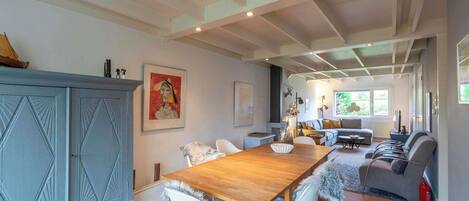 A spacious room with a wooden dining table, white chairs, a grey sofa, and a blue cabinet.
