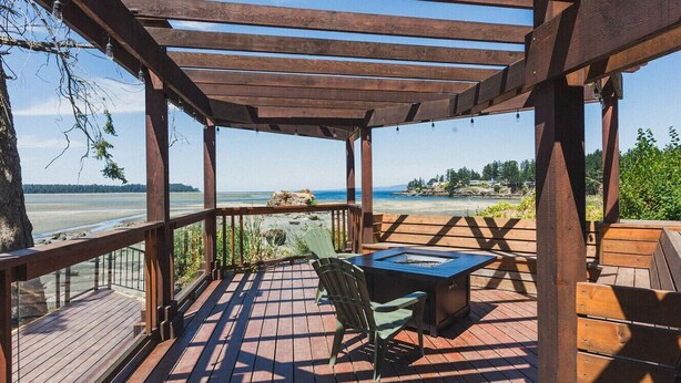 Een houten terras met een pergola, een tafel met stoelen en uitzicht op het strand.