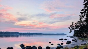 Vista de un lago con aguas tranquilas, orilla rocosa y una línea de árboles distante.