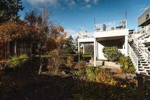 A covered outdoor area with a staircase leading to a second-floor balcony, surrounded by vegetation and trees.