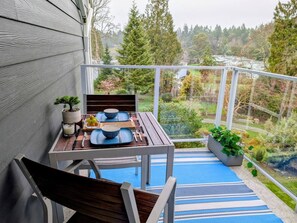 A balcony with a table set for two, a potted plant, and a view of a forested area.