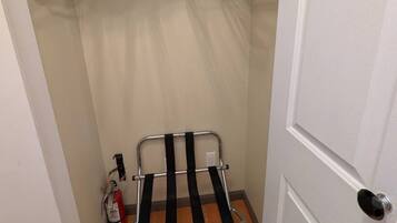 Une petite pièce avec une porte, un portant métallique avec des cintres et un extincteur.