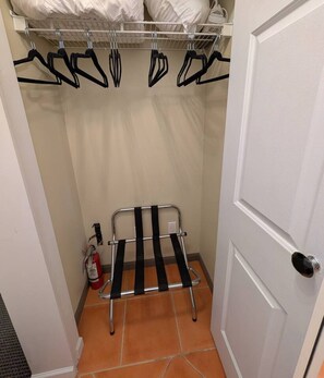 A small room with a door, a metal rack with hangers, and a fire extinguisher.