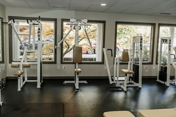 Un gimnasio con equipo de ejercicio, ventanas amplias y vistas al exterior.