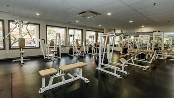 A gym with various exercise machines, benches, and large windows.