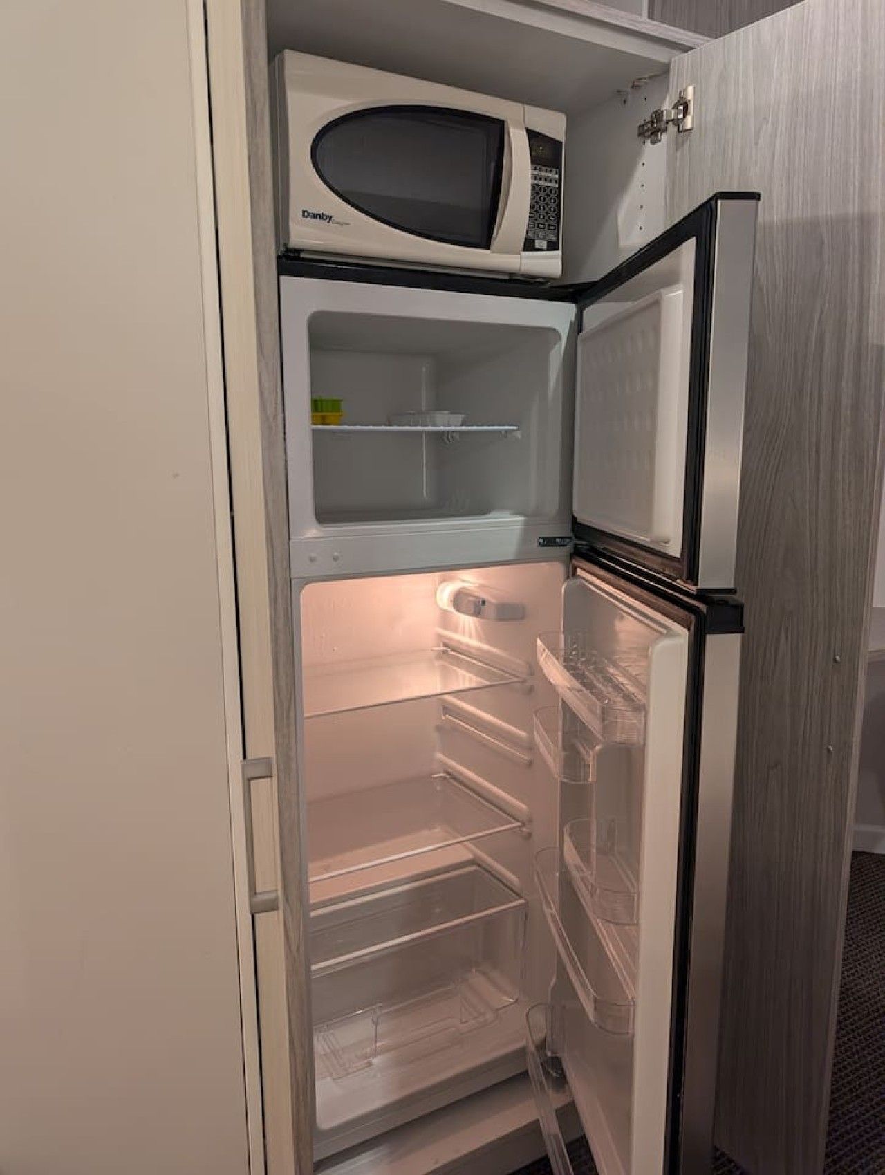 An open refrigerator with a microwave on top, clear shelves, and a freezer compartment.