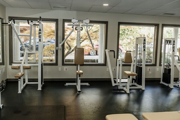 A gym with various exercise machines, large windows, and a black floor.