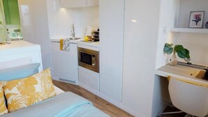 Een kleine slaapkamer met een bed, bureau en kitchenette.
