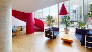 Een modern interieur met een rode spiraaltrap, houten vloeren en zithoeken met potplanten.