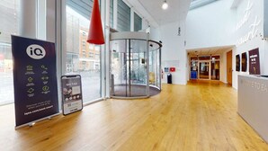 Een modern interieur met een houten vloer, een draaideur van glas en een bord met faciliteiten zoals een bioscoop en een fitnessruimte.