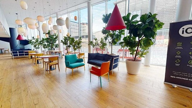 Ruime binnenruimte met houten vloeren, diverse zithoeken met banken en stoelen, en grote kamerplanten.