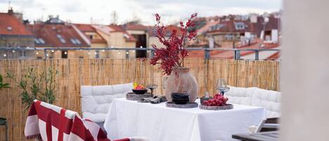 A rooftop terrace with a table set for dining, a decorative vase, and a view of the cityscape.
