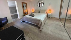 Quarto com cama, luminárias de cabeceira, espelho, cadeira e uma pequena mesa.
