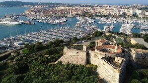 Paisagem costeira com uma fortaleza histórica, marina com vários barcos e edifícios urbanos densos.