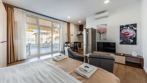 A hotel room with a bed, a TV, a desk, and a view of an outdoor pool area. - Lovely Studio With Seaview - Margarita (Ishëm)