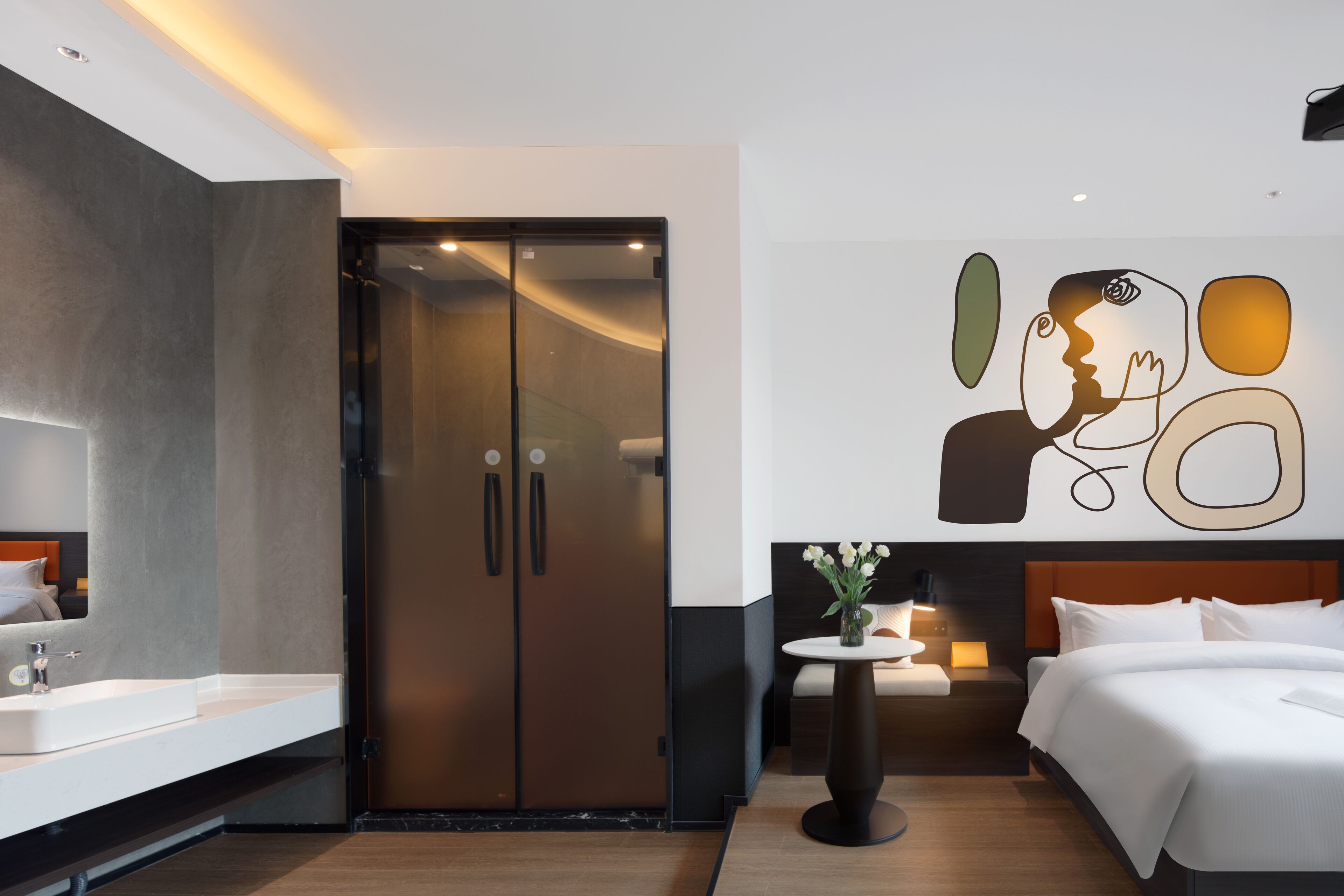 A modern hotel room with a large bed, a bathroom with a mirror and sink, and a wall with abstract art.