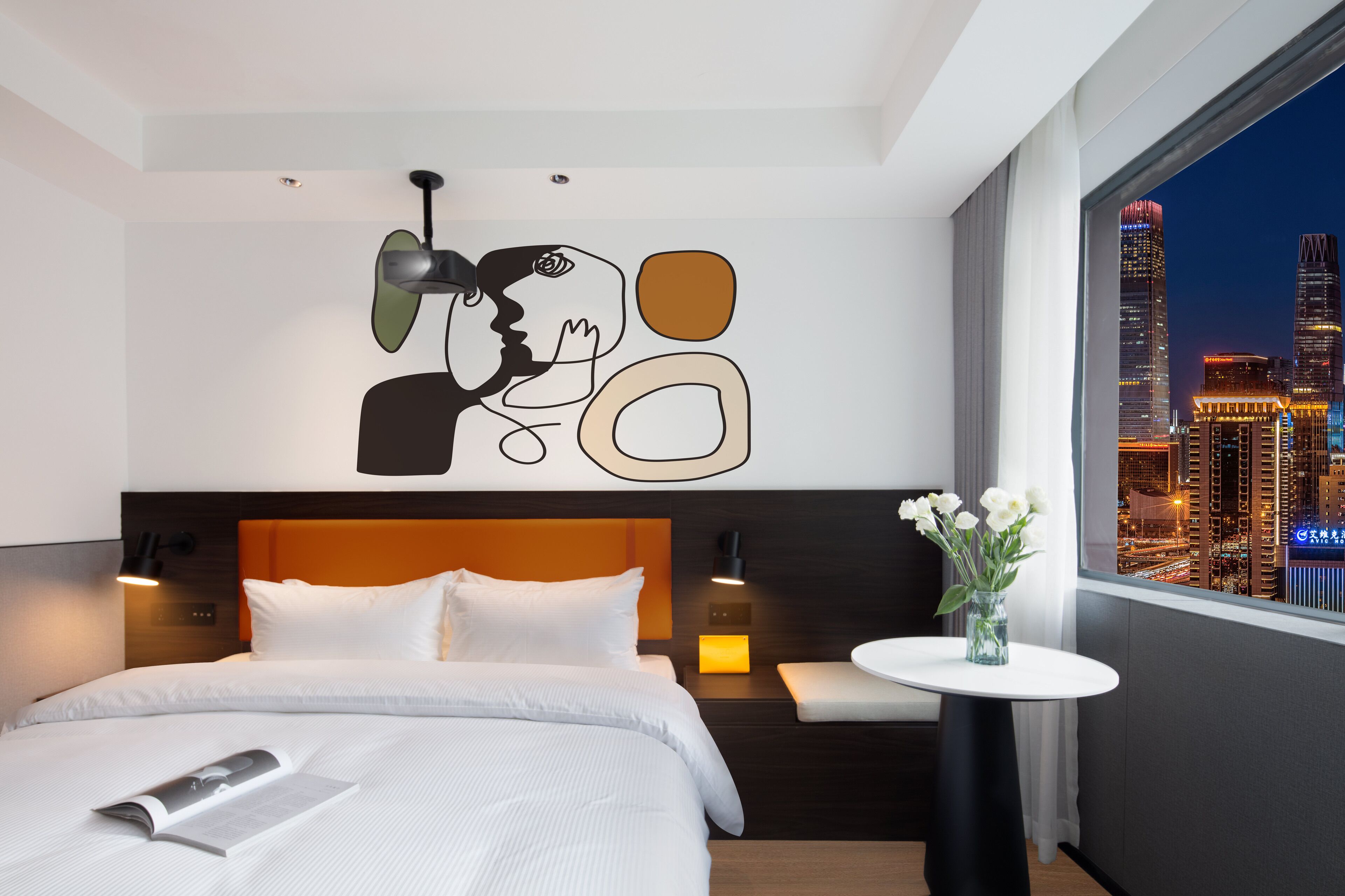 A modern hotel room with a large bed, a bedside table with a vase of flowers, a cityscape view, and a unique abstract wall art piece.