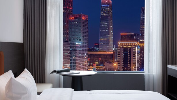 Una habitación de hotel con una cama, una mesita y vista a la ciudad de noche.