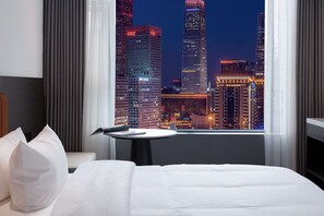 A hotel room with a bed, a small table, and a view of a cityscape at night. - Mcsrh Hotel-Guiyang Penshuichi (Guiyang)