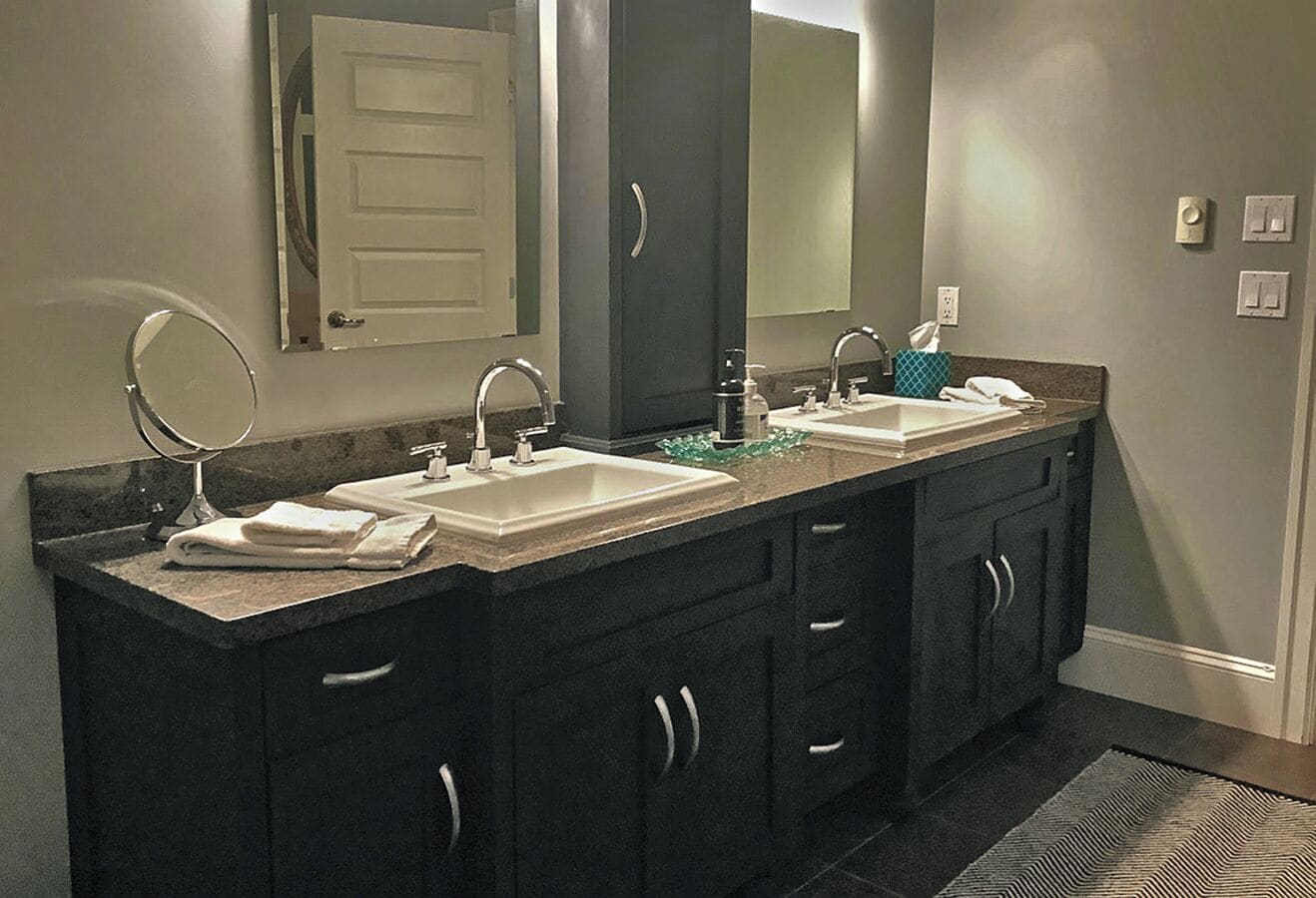 A bathroom with two sinks, dark cabinets, a mirror, and a towel rack.