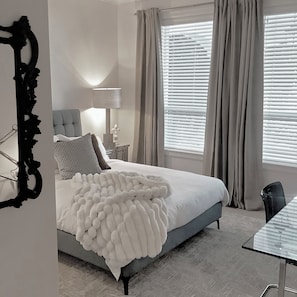 Een slaapkamer met een bed, een stoel, een lamp en een raam met gordijnen.