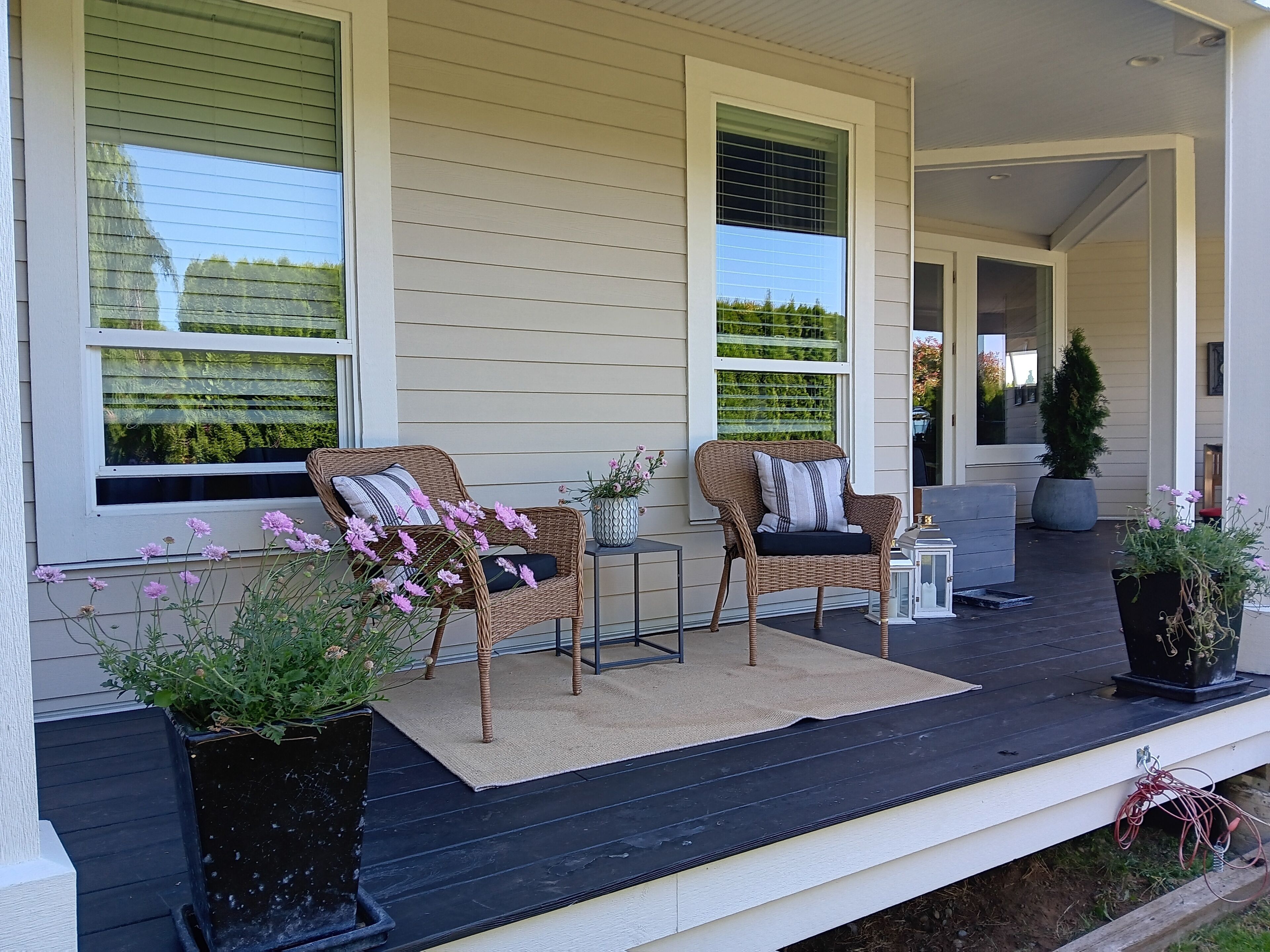 A covered porch with wicker chairs, a small table, and potted plants.