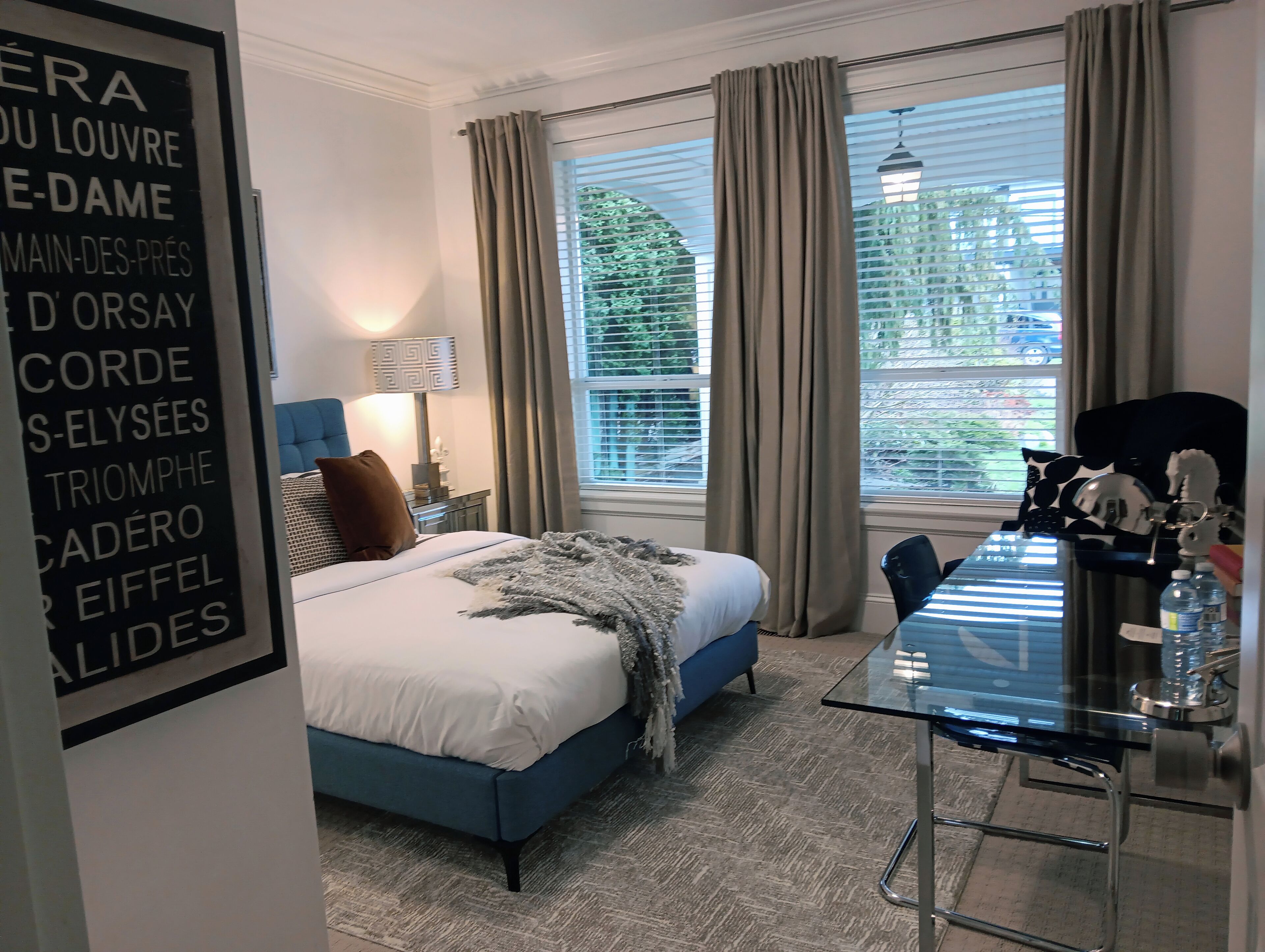 A hotel room with a bed, a desk, a lamp, and a window with curtains.