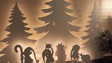 A room with a wooden floor, a wall with a cut-out Christmas tree design, and silhouettes of a cat, a dog, and a bird.