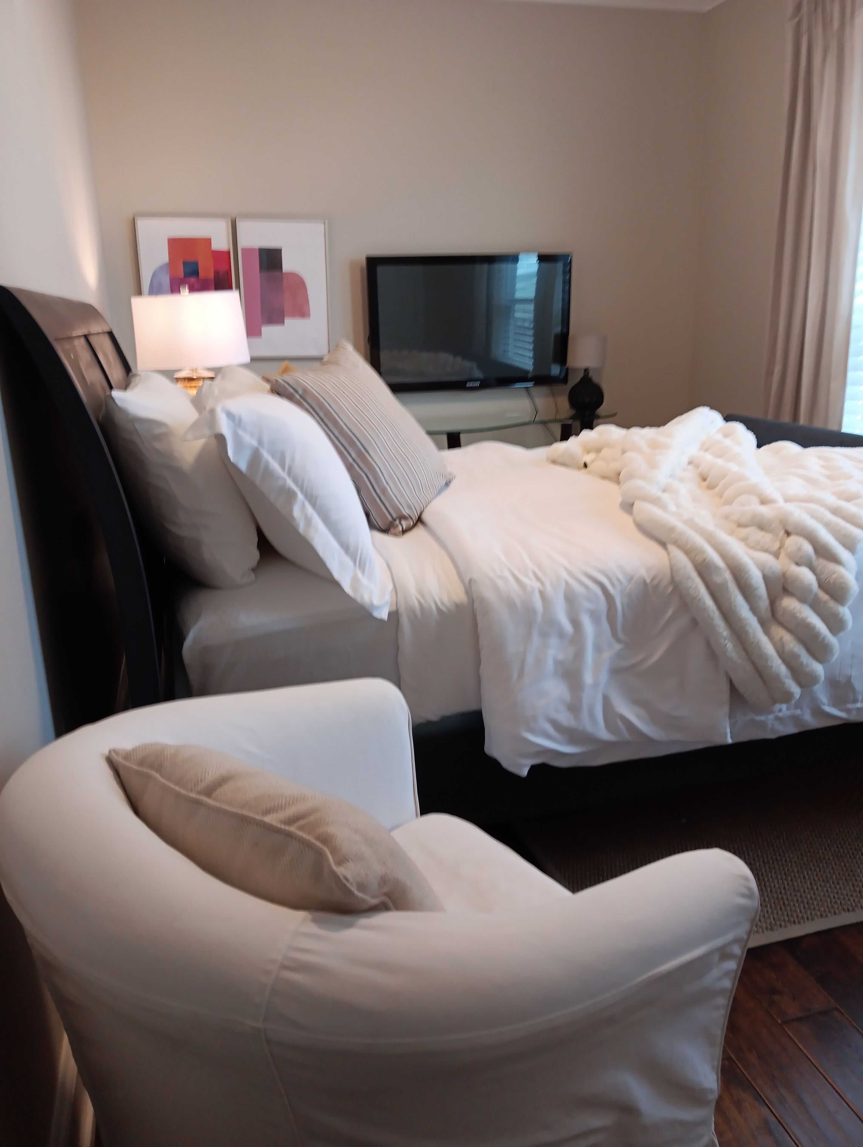 Habitación de hotel con cama, una silla, televisor y obras de arte en la pared.