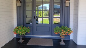 A dark grey front door with glass panels, two potted orange flowers, and a doormat on a black porch. - Sand and Salt Bed & Breakfast (White Rock)