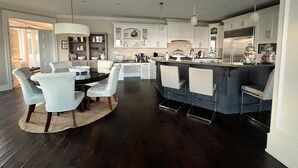 A modern kitchen with a central island, white cabinetry, and a dining area with a round table and chairs. - Sand and Salt Bed & Breakfast (White Rock)