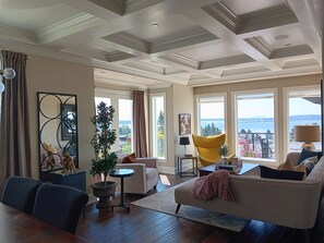 Un ampio soggiorno con una grande finestra vista mare, un divano accogliente, un tavolo da pranzo e una pianta in vaso.