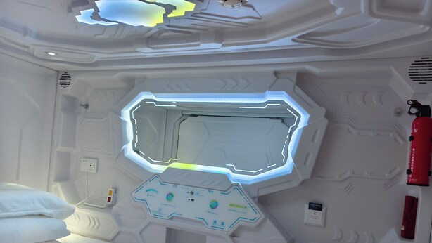 Um quarto futurista com um design geométrico na parede, um painel de controle e um extintor de incêndio.